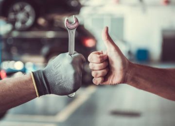 Cropped image of mechanics working in auto service. One is holding a spanner while the other is showing Ok sign